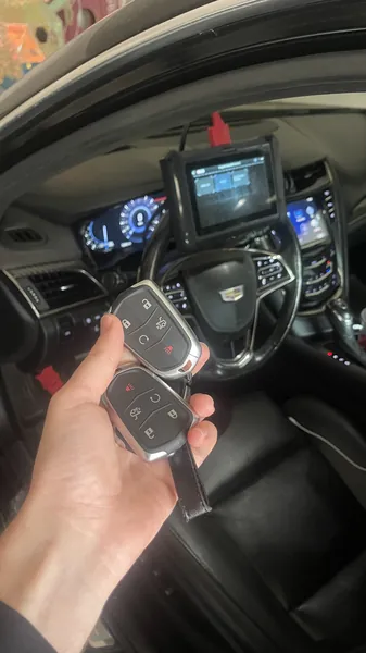 Two Cadillac smart keys held in front of a key programmer on the dashboard