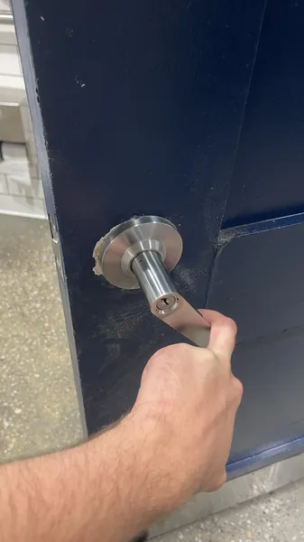 Hand testing a commercial lever lock with key cylinder on a navy steel door