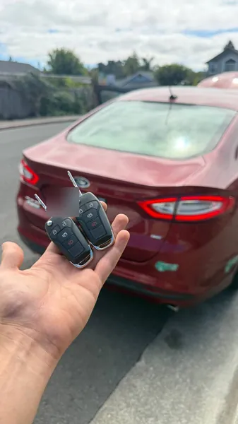 Two Ford flip keys held behind a red Ford sedan