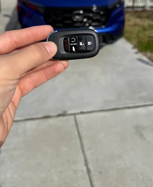 Honda smart key held in front of a blue Honda SUV