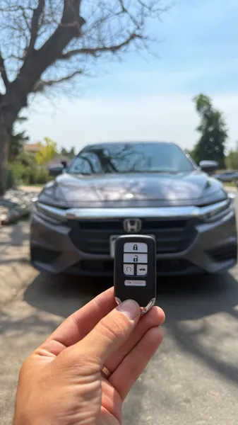 Honda smart key held in front of a gray Honda sedan