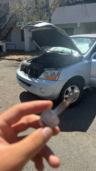 Car key held in front of a silver SUV with the hood open