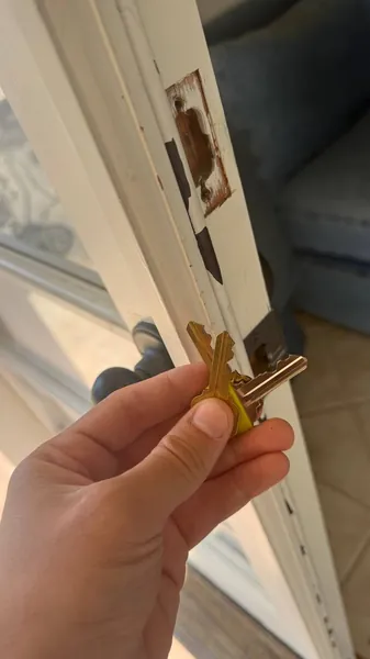 Keys held next to a damaged door edge where the old lock was