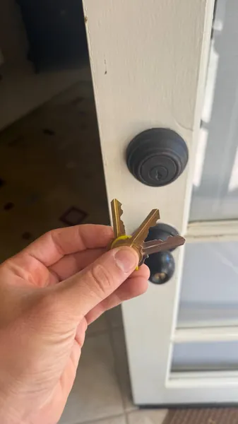 Two keys held next to a deadbolt and knob on a white door