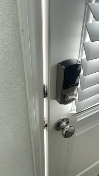 Kwikset smart deadbolt and round knob on a white door beside plantation shutters
