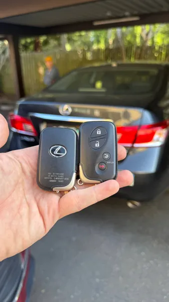 Two Lexus smart keys held behind a Lexus sedan