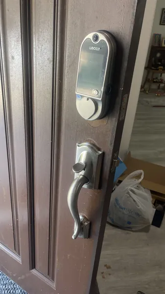 Lockly smart deadbolt with a built-in camera above a satin nickel handleset on a brown front door