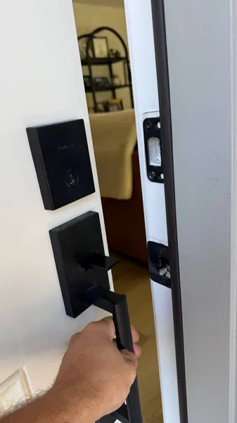 Hand on a matte black handleset below a matching deadbolt on a white front door