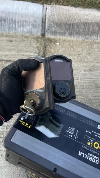 Worn Schlage touchscreen deadbolt taken off the door, held in a gloved hand