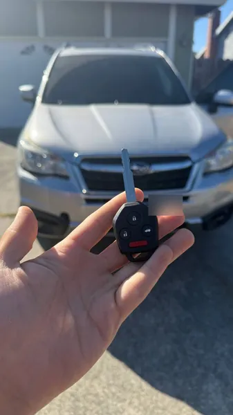 Subaru remote head key held in front of a silver Subaru SUV
